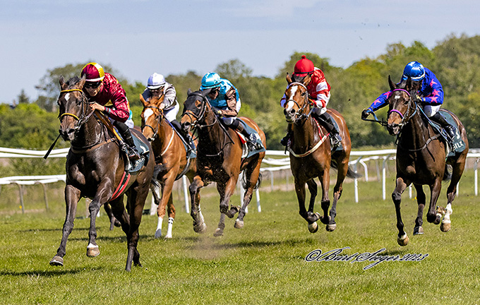 Lone Kaj Nielsens 3-årige Amicone (IRE) med jockey Elione Chaves
	på vej som den første over målstregen, lørdag den 20. maj 2023. Happy Feet i kobolt blå ses yderst til højre i billedetFoto Burg Seeger