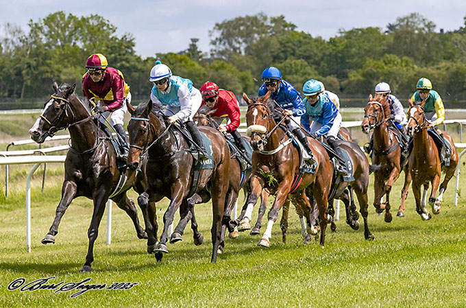 Bartholdi (USA) til venstre med bourgogne-gule farver i front med jockey Carlos Lopez på vej rundt Tribunesvinget, Klampenborg 7. juni 2025. Foto Burt Seeger